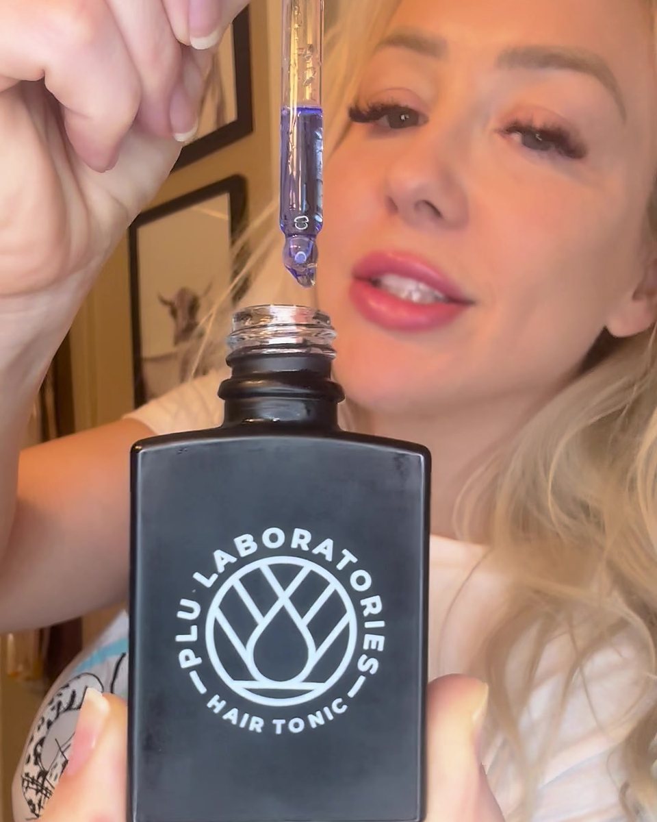 A creator holding the GHK-Cu Hair Tonic with the dropper raised